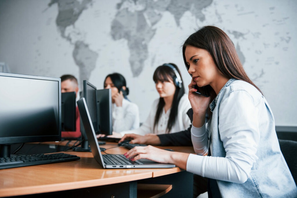 Employés d’un centre de contact d’une agence de voyages, travaillant sur ordinateurs et en communication avec des clients